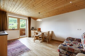 Une pièce avec un plafond en bois, une table à manger avec des chaises, un canapé et une vue sur un paysage verdoyant par la fenêtre.