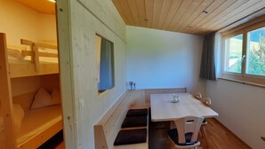 Une petite pièce agréable, dotée d’un lit superposé, d’une table avec des chaises et d’une fenêtre avec des rideaux.