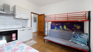 Une chambre compacte comprenant un lit superposé, un coin cuisine et un petit espace salon.