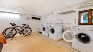 Une buanderie avec un vélo, trois machines à laver et une fenêtre.