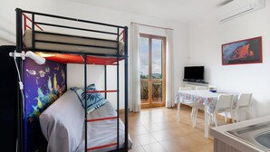 Un lit superposé avec une couvre-lit colorée, une table à manger avec des chaises, un téléviseur et une porte-fenêtre donnant sur un balcon.