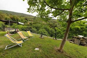 Uma área ao ar livre com gramado, cadeiras de descanso e uma estrutura de pedra.