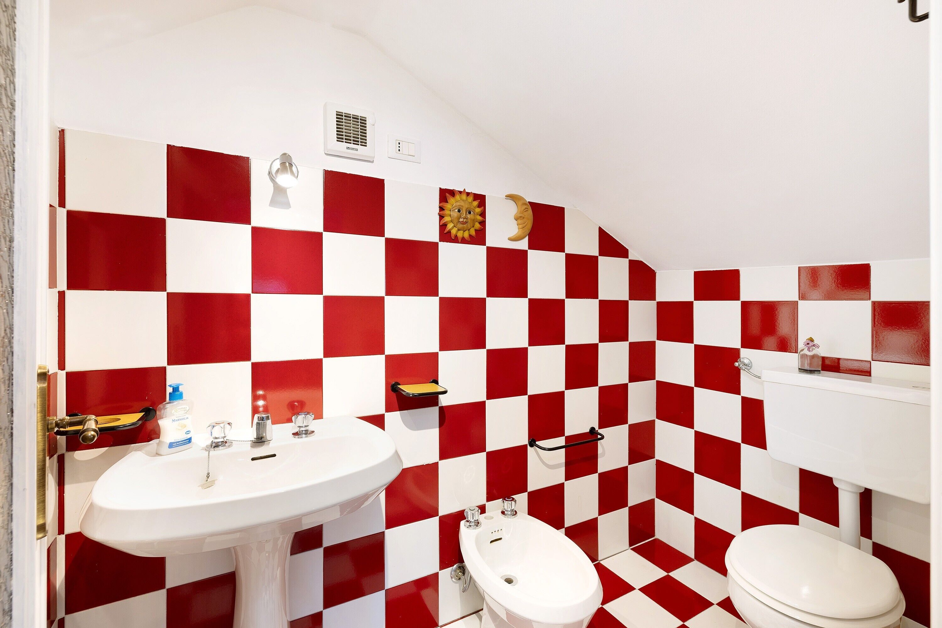 Une salle de bain avec un carrelage rouge et blanc à carreaux, un lavabo blanc, un bidet et des toilettes.