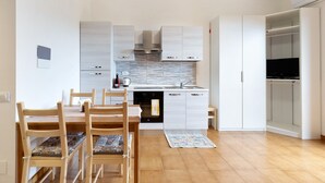 A modern kitchen with white cabinetry, a built-in oven, and a dining area with wooden chairs and a table. - Apartment 'Elena E Joerg 2' with Mountain View, Shared Garden and Wi-Fi (Vezzi Portio)