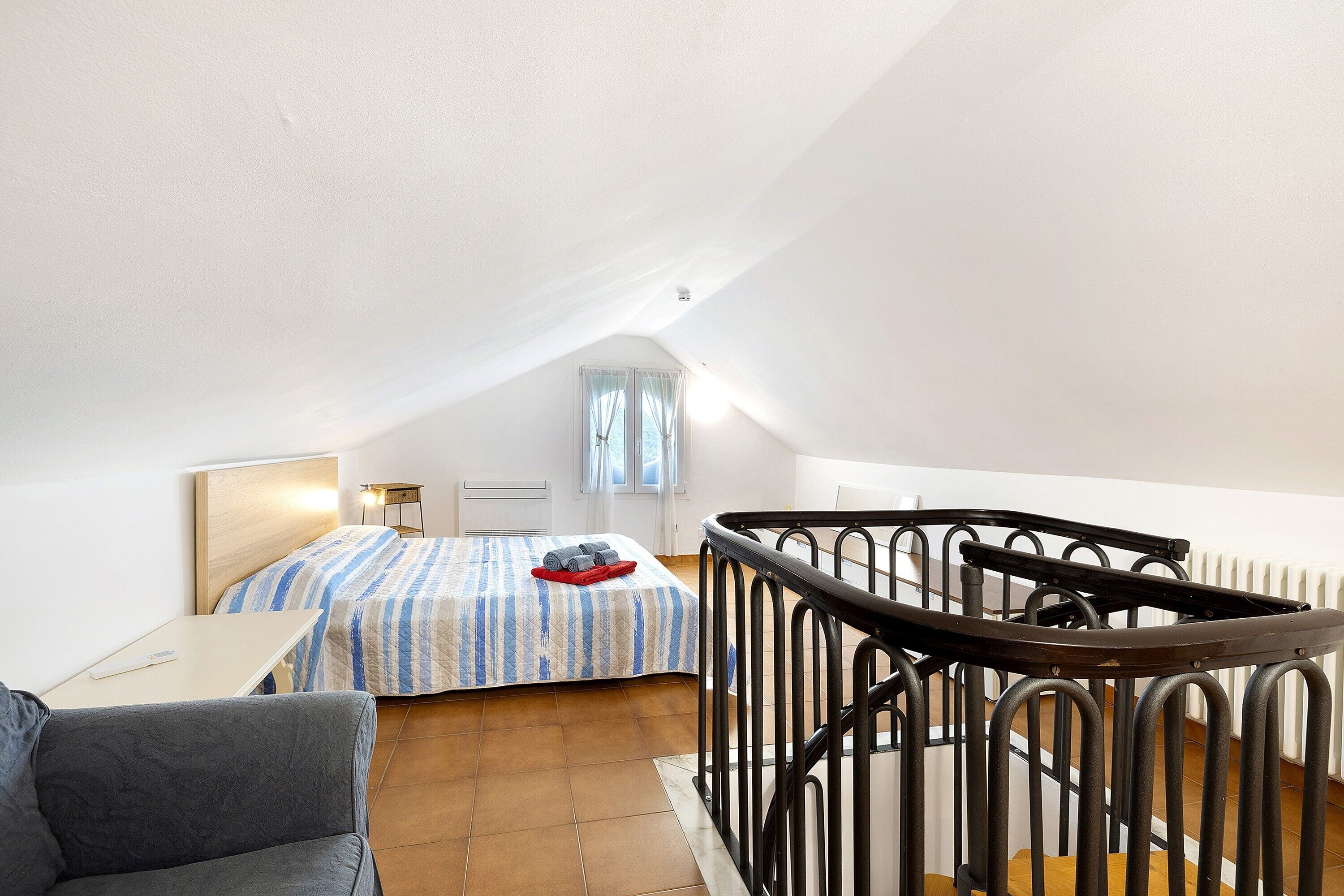 Una camera da letto con un letto, una scrivania, una sedia e una scala con ringhiera.