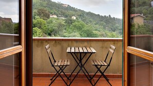 A balcony with two wooden chairs and a table, overlooking a hillside with houses. - Apartment 'Elena E Joerg 2' with Mountain View, Shared Garden and Wi-Fi (Vezzi Portio)