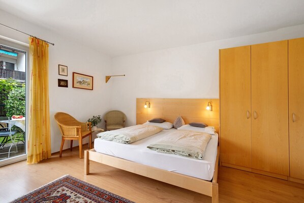 A bedroom with a bed, wooden wardrobe, two chairs, a small table, and a window with curtains. - Apartment 'Das Landhaus Apt Pink Lady' with Mountain View, Private Terrace and Wi-Fi (Terlano)