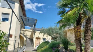 A residential building with a staircase, a palm tree, and a garden with purple flowers.