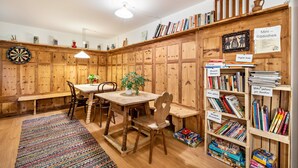 Een gezellige kamer met een houten tafel, stoelen, een boekenplank en een dartbord.