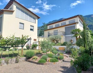 Un bâtiment à deux étages, doté d’un jardin à l’avant, comprenant une zone pavée et diverses plantes.