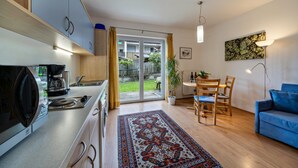 Een moderne keuken met een koffiezetapparaat, een eethoek met een tafel en stoelen, een blauwe bank en een groot raam met gordijnen.