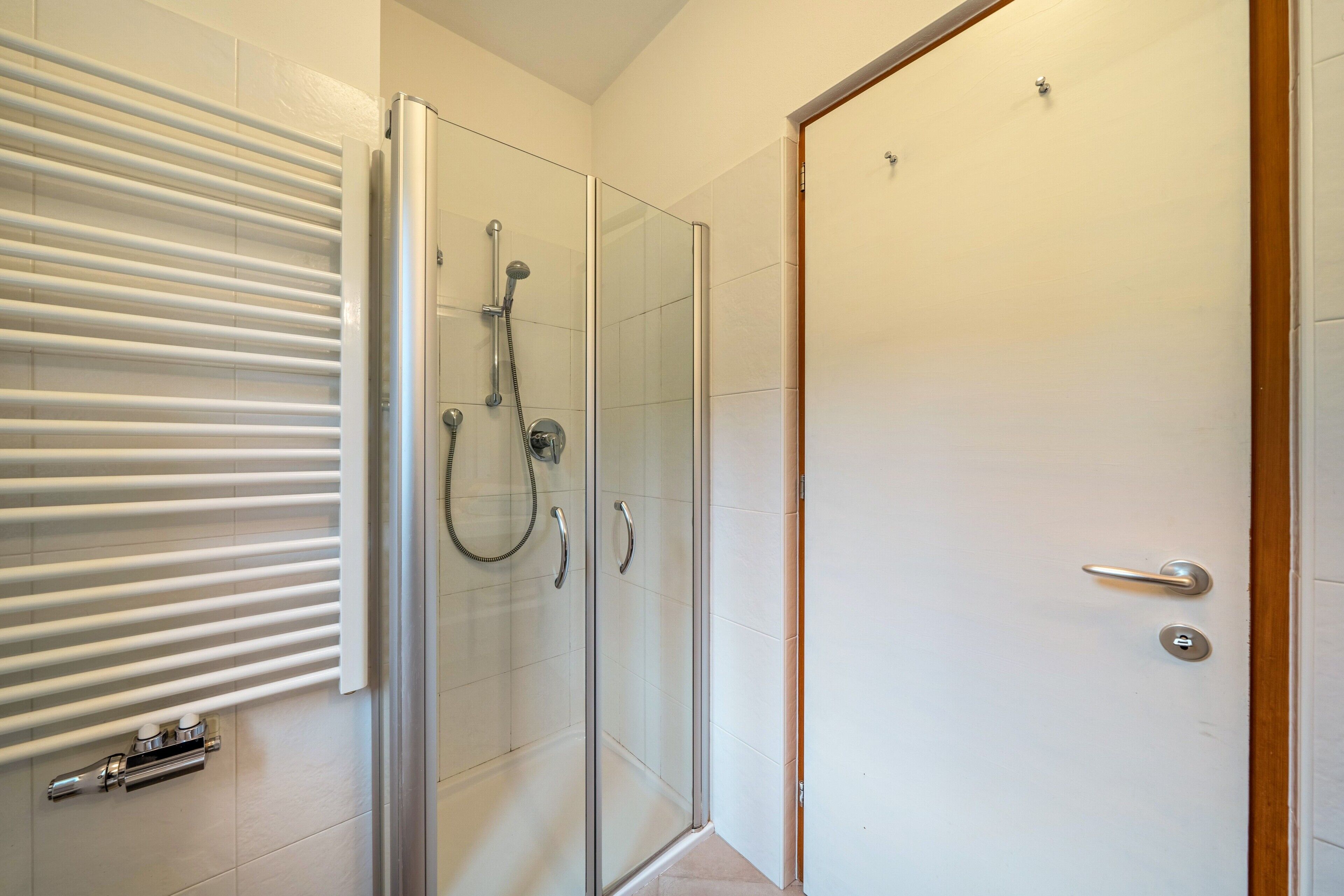 A glass-enclosed shower with a handheld showerhead, a glass door, and a towel rack with towels.