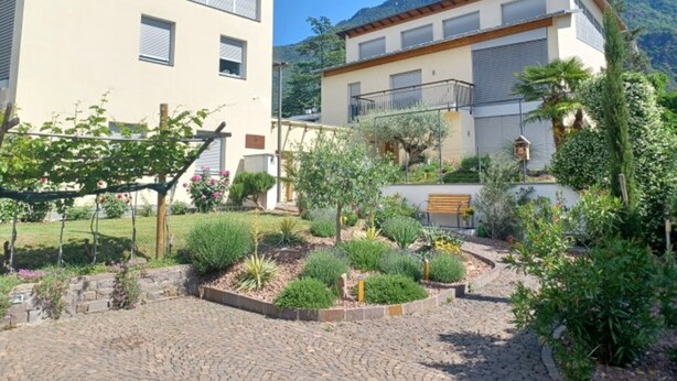 Un bâtiment à deux étages, doté d’un jardin à l’avant, comprenant une zone pavée et diverses plantes.
