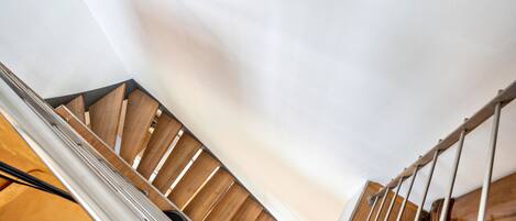 A wooden staircase with metal railings and a white wall.