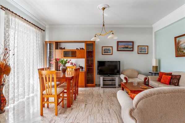 Un salon comprenant un téléviseur, un canapé et un coin repas avec des chaises et une table.