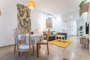 A modern living room with a dining area, a sofa, a coffee table, and a TV mounted on the wall.