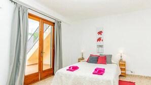 A bedroom with a bed, a red rug, a wooden door, and a wall-mounted artwork. - Holiday Home 'Puig' with Mountain View, Wi-Fi and Air Conditioning (Pollensa)