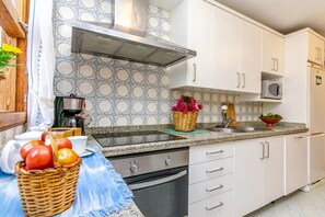 Una cocina con gabinetes blancos, una campana extractora de acero inoxidable, un microondas y un fregadero.