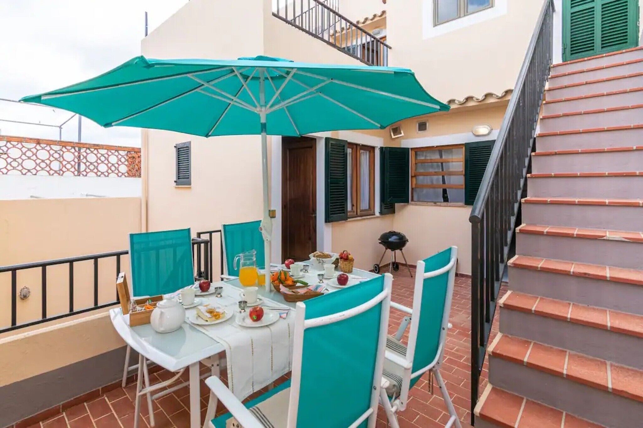 Un comedor con una mesa lista para el desayuno, un paraguas verde y una escalera.