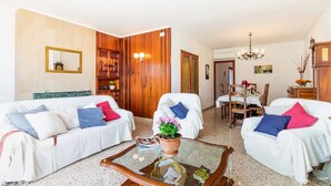 A hotel room with two white sofas, a coffee table, a bookshelf, a dining area with a table and chairs, and a chandelier. - Holiday Home 'Puig' with Mountain View, Wi-Fi and Air Conditioning (Pollensa)