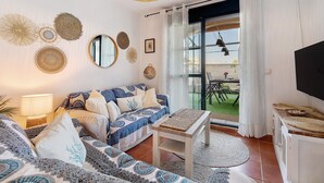 Una sala de estar con sofá, mesa, televisor y balcón con mesa y sillas.