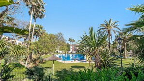 Una piscina rodeada de palmeras y una valla, con edificios al fondo.