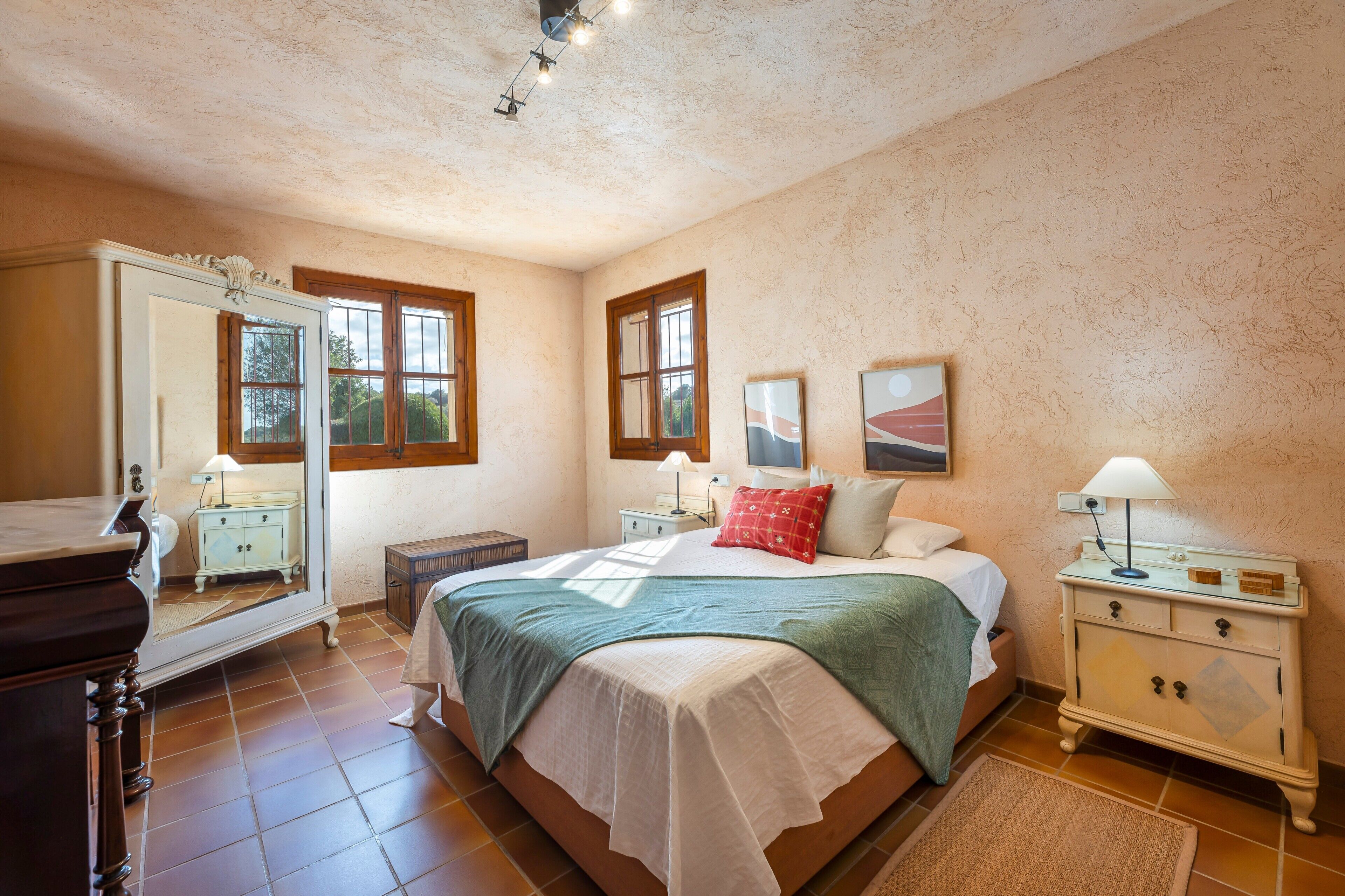 A bedroom with a bed, nightstands, a dresser, a mirror, and a window.