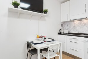 Une petite cuisine équipée avec un téléviseur, des placards blancs, un plan de travail et un coin repas comprenant une table et des chaises.