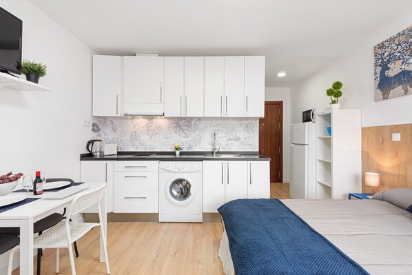 Une pièce de taille modeste comprenant un lave-linge, un lit, une table à manger et un coin cuisine.