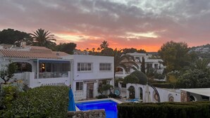 Zona residencial com piscina, edifícios brancos e céu ao pôr do sol.