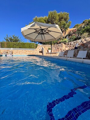 En swimmingpool med krystalklart blåt vand, omgivet af liggestole og en stenvæg.