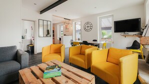 Ein modernes Wohnzimmer mit Sofa, Couchtisch mit Buch, Fernseher und Essbereich mit Stühlen.
