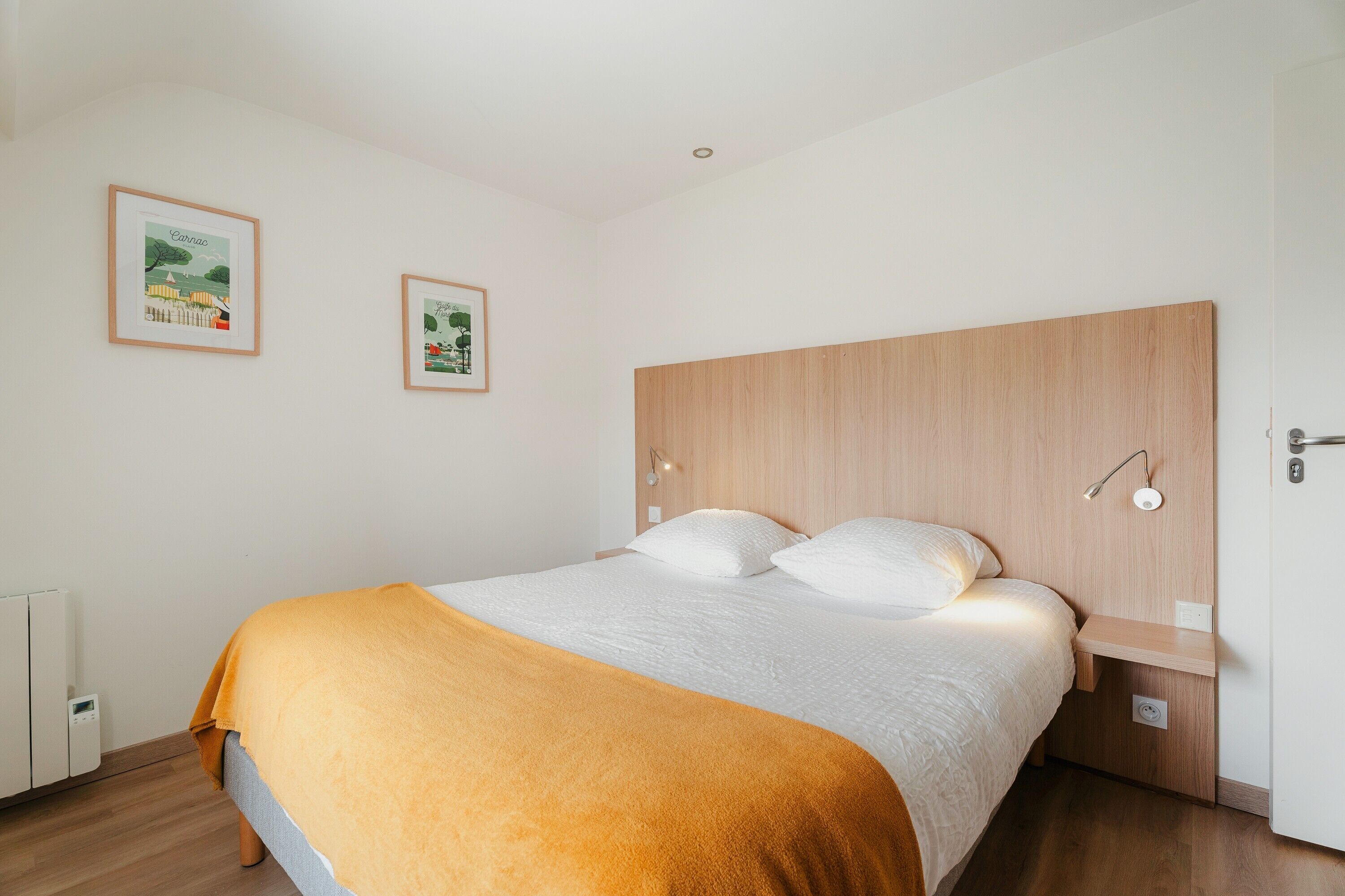 A bedroom with a bed, a headboard, a bedside table, and two framed pictures on the wall.