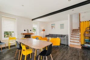 A modern living space with a dining area, sofa, staircase, and a view of the outdoors.