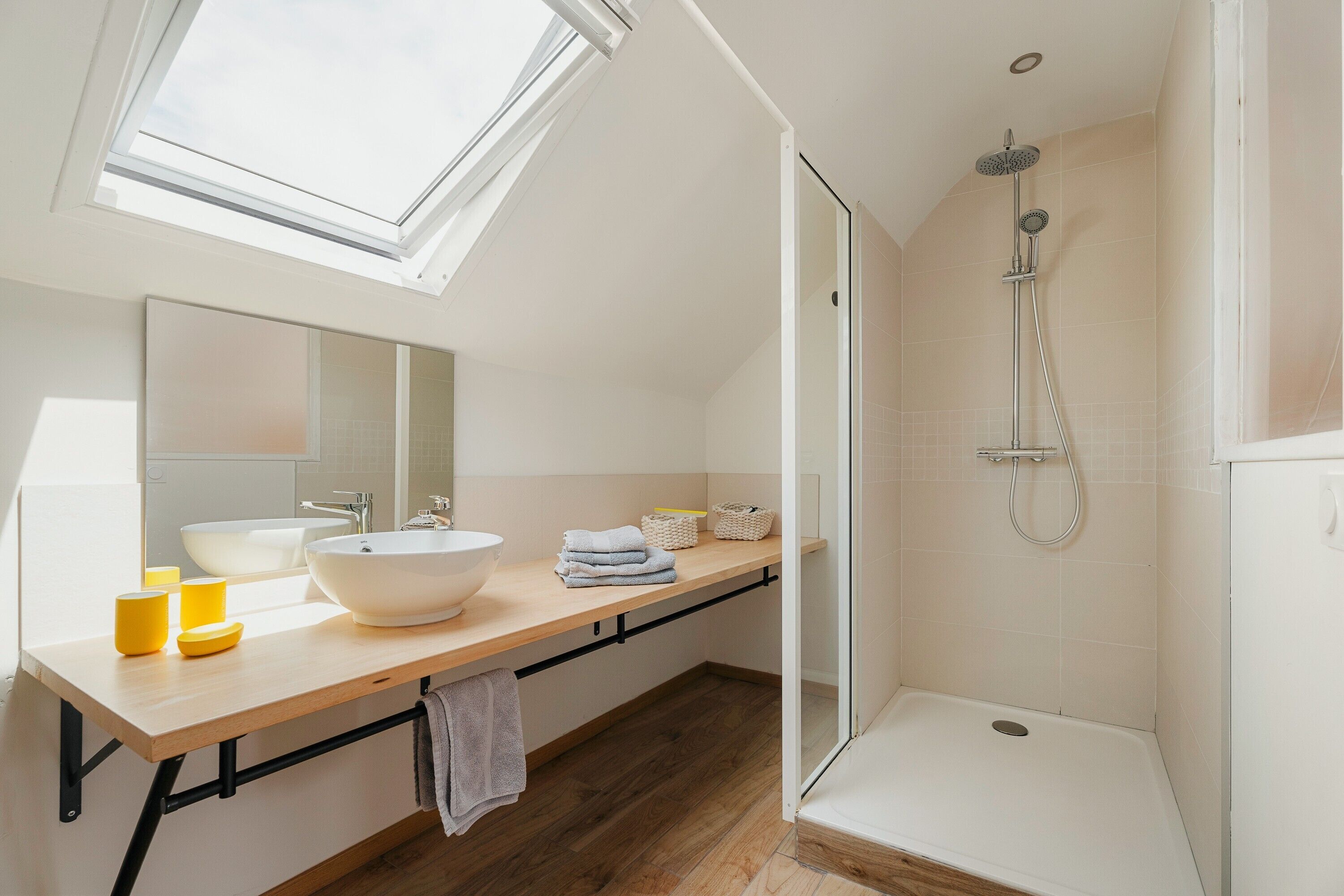 A modern bathroom with skylights, a large sink, a shower, and a wooden vanity.