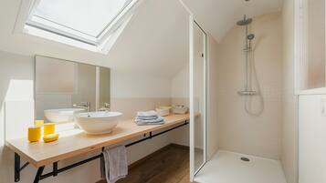 A modern bathroom with skylights, a large sink, a shower, and a wooden vanity.
