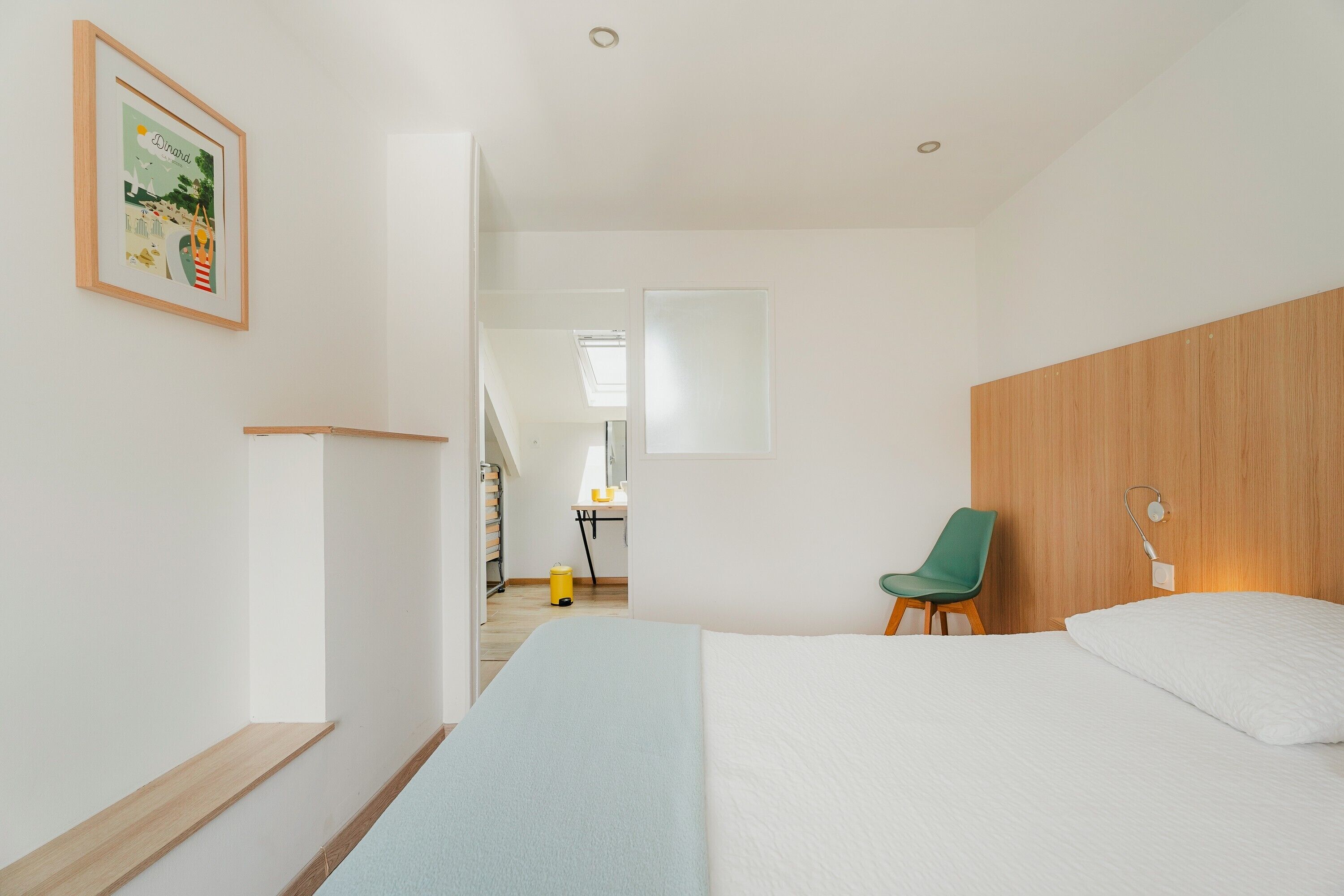 Una habitación de hotel moderna con una cama, una silla verde, un cabecero de madera, un cuadro enmarcado en la pared y una escalera que lleva a otra habitación.