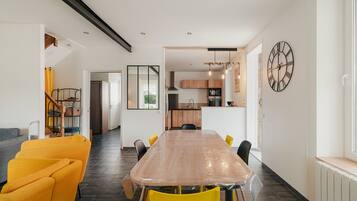 Une cuisine moderne dotée d’un grand îlot central, d’un coin repas avec une longue table et des chaises jaunes, et d’une horloge bien visible au mur.