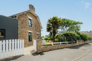 A stone building with a white picket fence, a palm tree, and a clear sky.