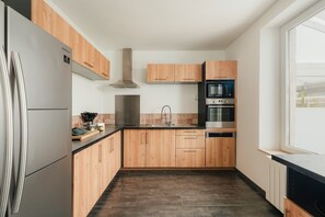 A modern kitchen with wooden cabinets, stainless steel appliances, and a black countertop. - Holiday Home 'Gîte De La Tour' with Private Garden and Wi-Fi (PLOUBALAY)