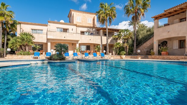 A swimming pool with lounge chairs, palm trees, and a building with a tiled roof.