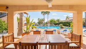 A covered outdoor seating area with a pool view, wooden furniture, and a ceiling fan.