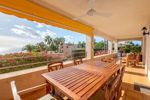 Una mesa y sillas de madera bajo un toldo amarillo, con vistas a un balcón y al mar, con palmeras.