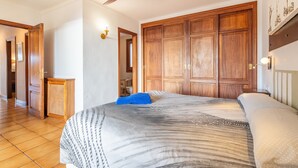 Un dormitorio con una cama grande, armario de madera, ventilador de techo y un pasillo que conduce a otra habitación.