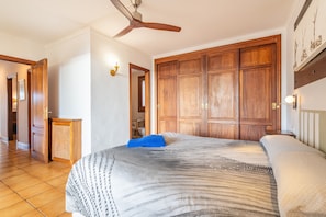 A bedroom with a large bed, wooden wardrobe, ceiling fan, and a hallway leading to another room.