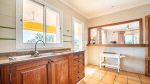 Una cocina con armarios de madera, un fregadero, una ventana con vistas y un estante blanco pequeño.