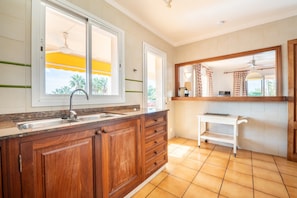 A kitchen with wooden cabinets, a sink, a window with a view, and a small white shelf.