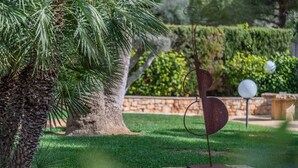 Un jardín con una palmera, una escultura de metal y un banco de piedra.