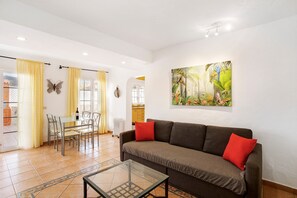 A living room with a sofa, a glass coffee table, a dining table with chairs, and a painting on the wall.