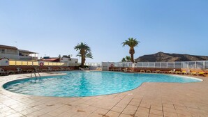 Une piscine avec une terrasse carrelée, des palmiers et une vue sur une montagne.